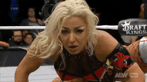 a woman is kneeling down in a wrestling ring with a sign that says draft kings on it .
