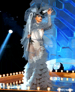 a woman in a white dress with ruffles and a hat is on a stage