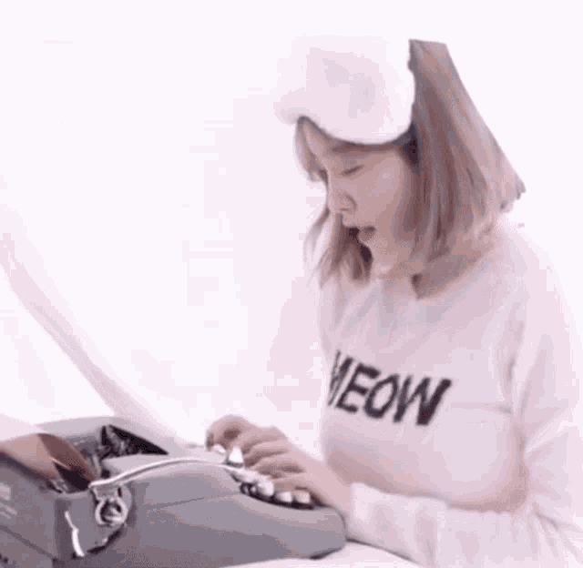a woman wearing a pink sweater that says meow is typing on an old typewriter .