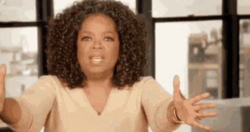 oprah winfrey is standing in front of a window with her arms outstretched and making a funny face .