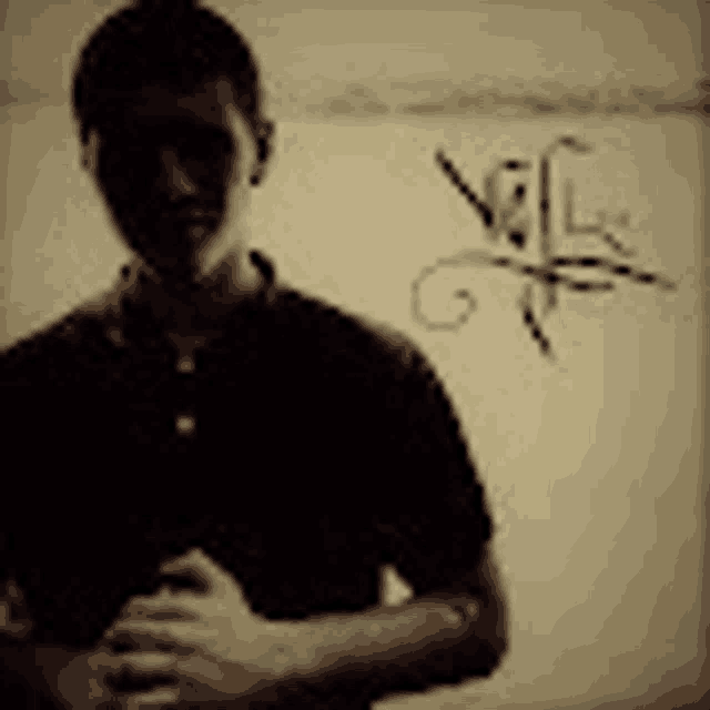 a man in a black shirt is standing in front of a white wall with a drawing on it .