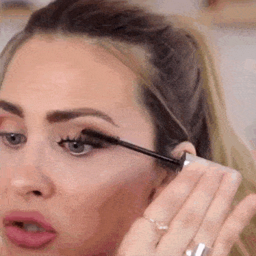 a close up of a woman applying mascara to her eye