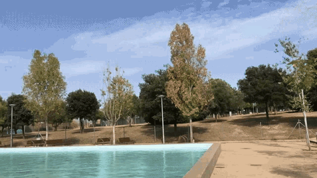 a swimming pool in a park with trees and benches in the background