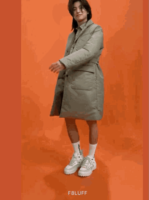 a man wearing a coat and shorts is standing in front of an orange background with the word f8luff on it