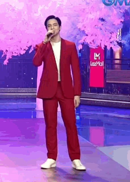 a man in a red suit is singing into a microphone while standing on a stage .