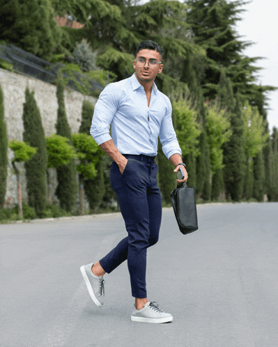 a man in a light blue shirt and blue pants is walking down the street holding a black briefcase