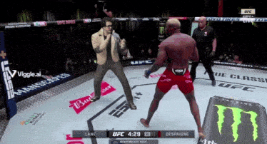 a man in a suit stands in a boxing ring while a man in red shorts stands in the corner