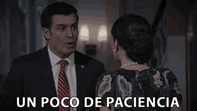 a man in a suit and tie is talking to a woman who is wearing a dress and pearls .