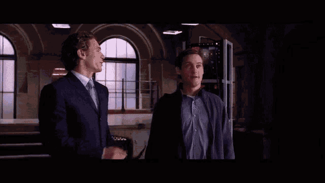 three men are standing in front of a window and talking to each other in a dark room .