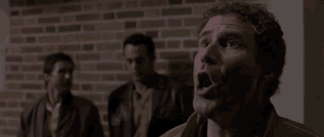 a man with his mouth open is standing in front of a brick wall with two other men .