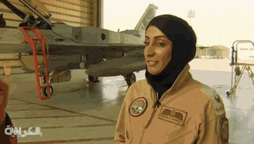 a woman in a military uniform stands in front of a fighter jet with cnn written on the bottom