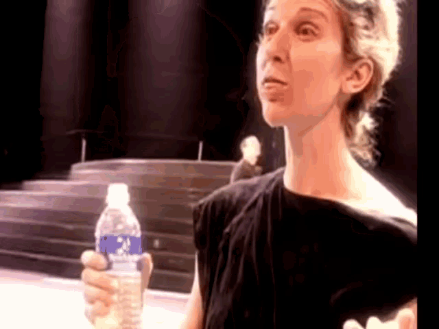 a woman in a black shirt is holding a bottle of water with a blue label