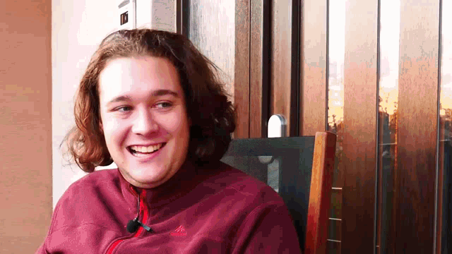 a young man wearing a maroon adidas jacket is smiling
