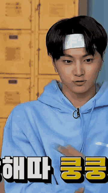 a young man wearing a headband and a blue hoodie is standing in front of yellow lockers .