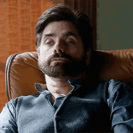 a man with a beard is sitting in a chair with his eyes closed .