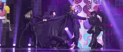 a group of people are dancing on a stage with purple lights behind them .
