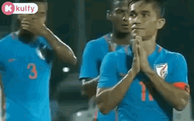 a group of soccer players are standing on a field with their hands folded in prayer