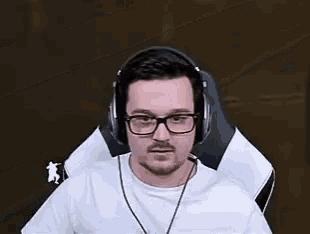 a man wearing glasses and headphones is sitting in a chair and looking at the camera .