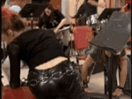 a woman in black leather pants is kneeling down in front of a drum set in a room .