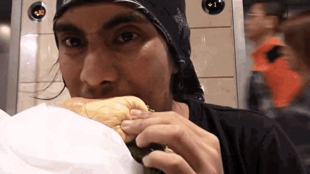 a man with a bandana on his head is eating a sandwich in an elevator