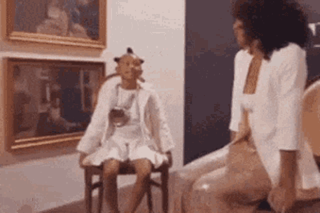 a woman is sitting on a chair next to a child in a white dress in a museum .