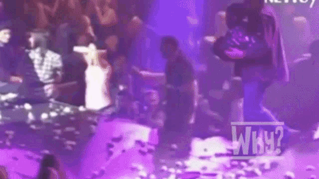 a man is standing on a stage in front of a crowd in a club with purple lights .
