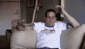 a man in a white shirt is sitting on a couch with his arms outstretched and his head in the air .