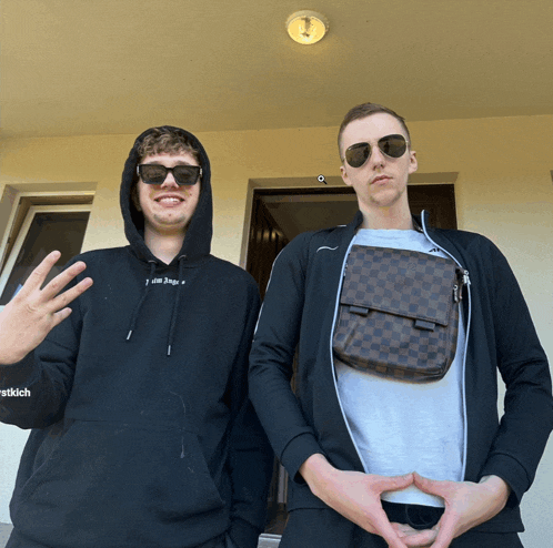 a man wearing a black hoodie that says palm angels is standing next to another man wearing sunglasses