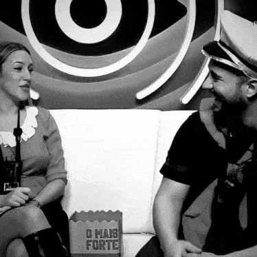 a man and a woman sit on a couch with a box that says o mais forte on it