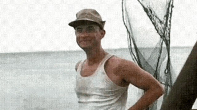 a man wearing a hat and a tank top is standing on a boat in the ocean .