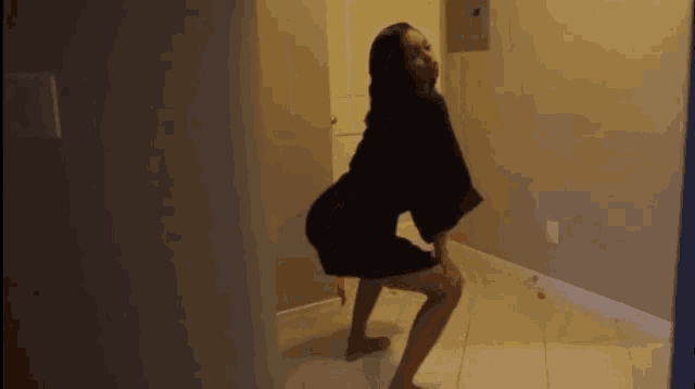 a woman in a black robe is squatting on a tiled floor