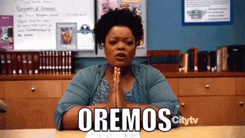 a woman sits at a desk with her hands folded in front of a sign that says oremos