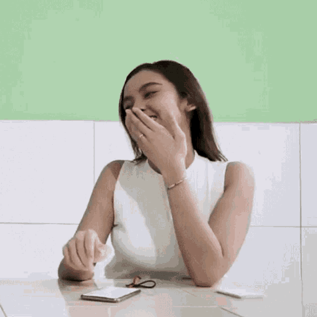 a woman is sitting at a table with her hands on her face and making a funny face .