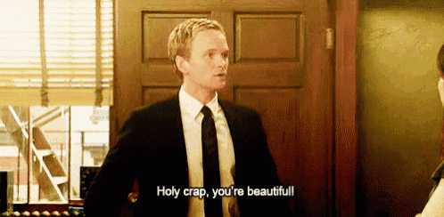 a man in a suit and tie is standing in front of a door and saying holy crap , you 're beautiful .