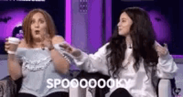 two women are sitting next to each other on a couch with their hands in the air .