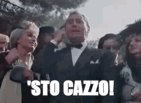 a man in a tuxedo is standing in front of a crowd of people and saying ' sto cazzo ! ' .