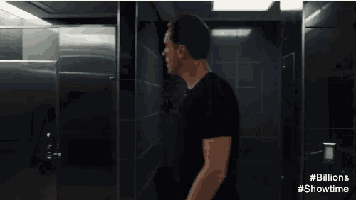 a man in a black shirt is walking in a bathroom with the words # billions #showtime on the bottom