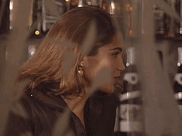 a woman in a brown jacket is smiling in front of bottles