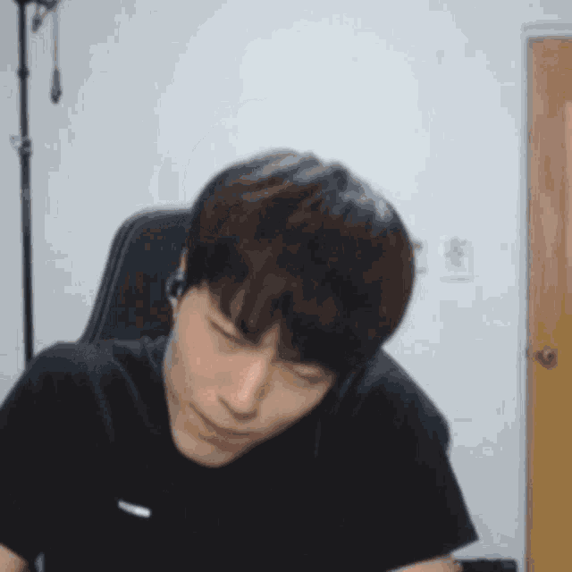 a man in a black shirt is sitting in a chair with his eyes closed and headphones on .