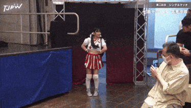 a woman in a cheerleader outfit is standing in front of a tjpw sign