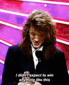 a man with long hair is talking into a microphone and says i didn 't expect to win anything like this