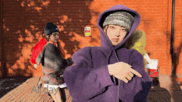 a woman wearing a purple hoodie and a black beanie is pointing at something
