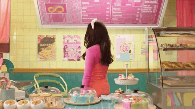 a woman stands in front of a bakery house menu