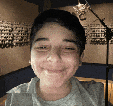 a young boy smiles in front of a microphone in a recording studio