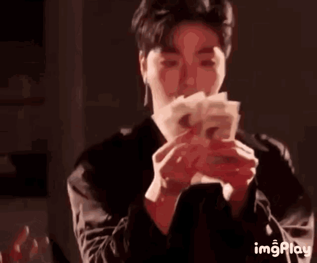 a man is holding a bunch of money in his hands in front of his face .