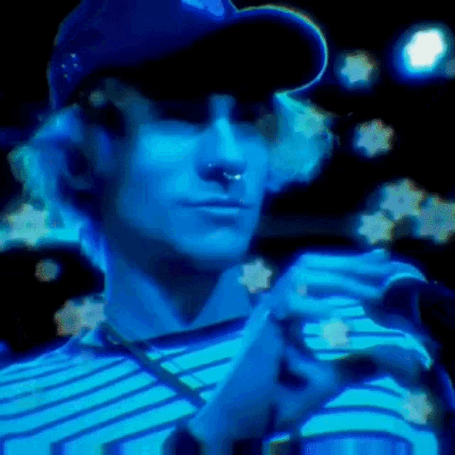 a man wearing a baseball cap and a nose ring is holding a microphone in a dark room .