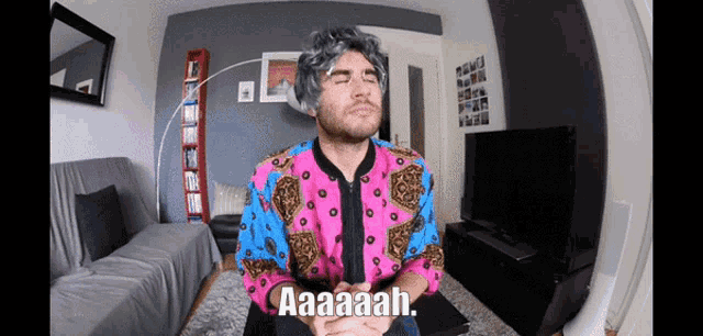 a man in a colorful shirt is sitting in a living room with his eyes closed and says aaaaah