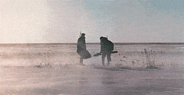 two men are standing in the middle of a snowy field looking at something