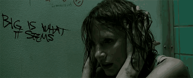a woman is covering her ears in front of a wall that says big is what it seems
