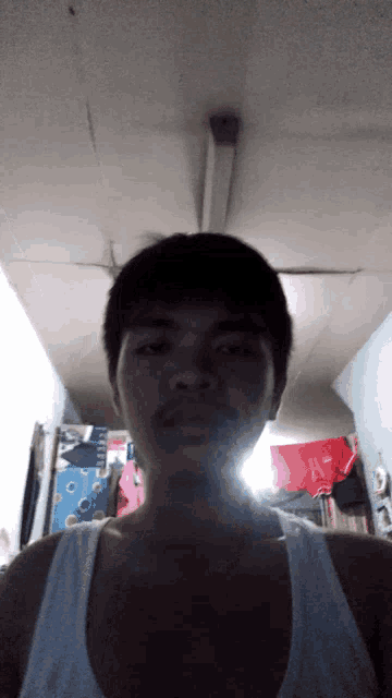 a man wearing a white tank top is standing in a dark room